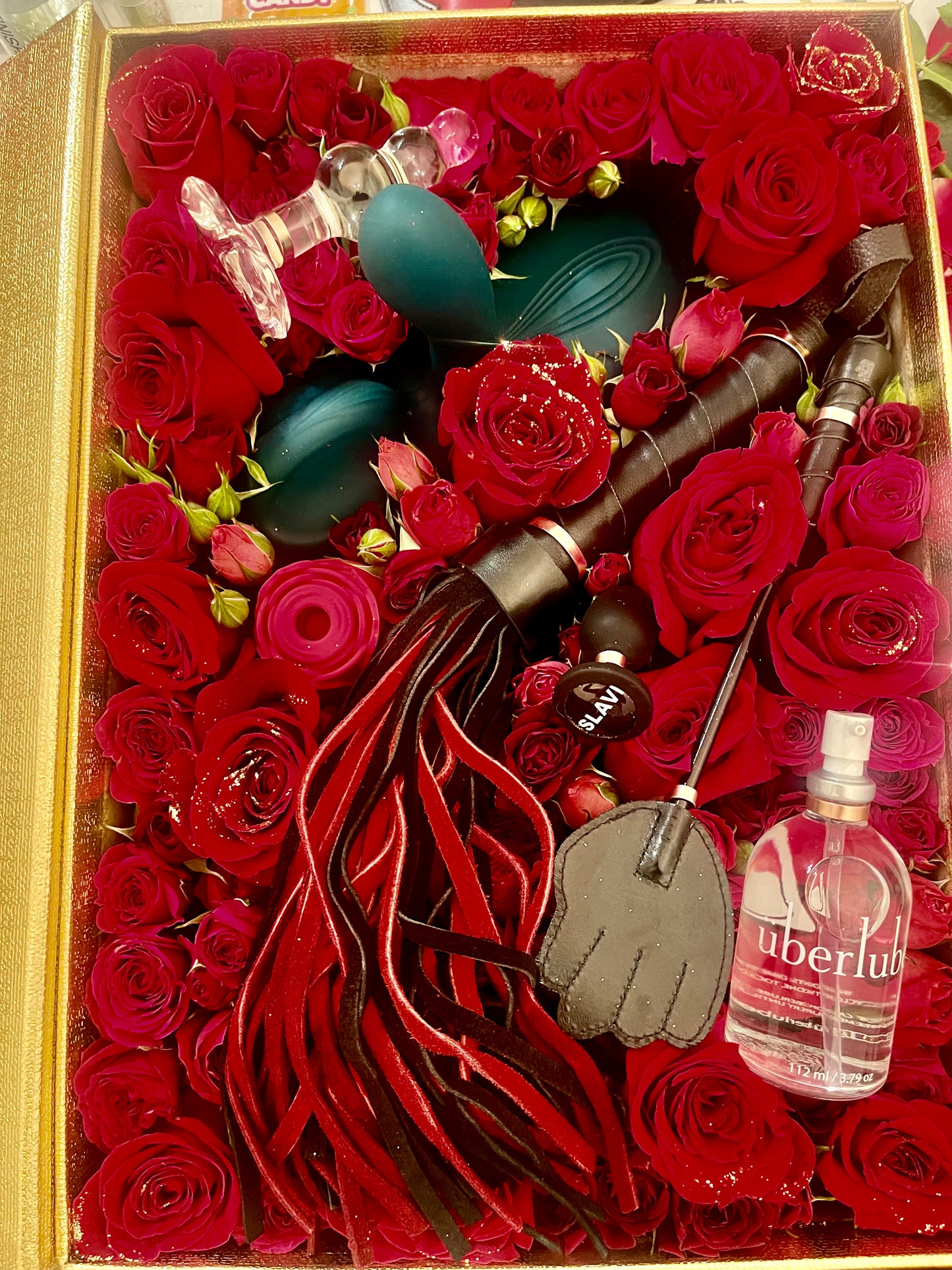 Decorative box with red roses, a tassel, and a bottle labeled 'uberlud'.